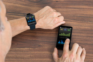 Close-up Of Mature Man With Smartwatch And Cellphone Showing Heartbeat Rate Sitting At The Table