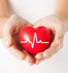 health, medicine and charity concept - closeup of female hands holding red heart with ecg line